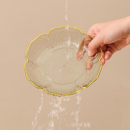 Clear glass bowl with gold rim being filled with water from a faucet on a beige background