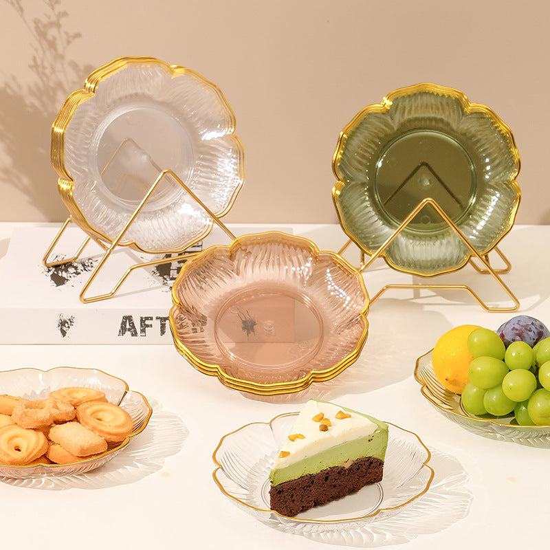 Decorative glass plates with gold rims on stands, surrounded by snacks and fruits.
