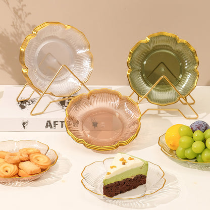 Decorative glass plates with gold rims on stands, surrounded by snacks and fruits.