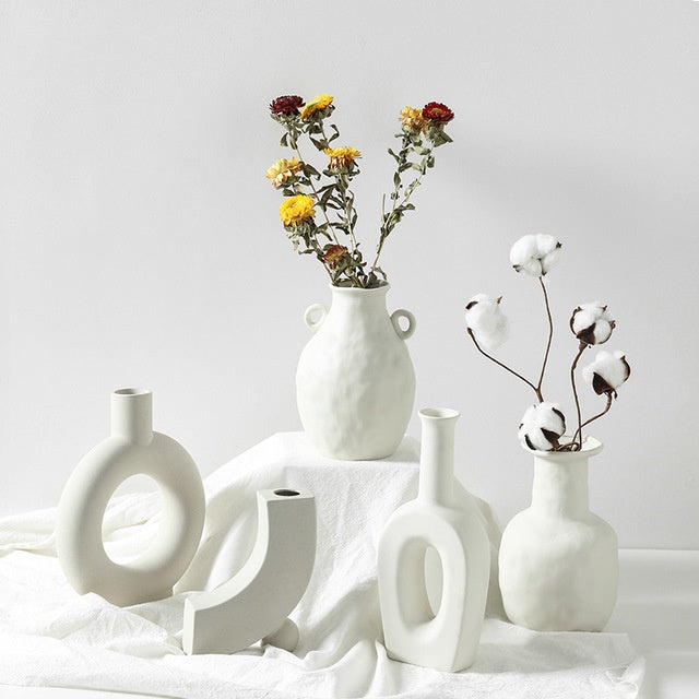 Collection of white ceramic vases with dried flowers on a light gray background