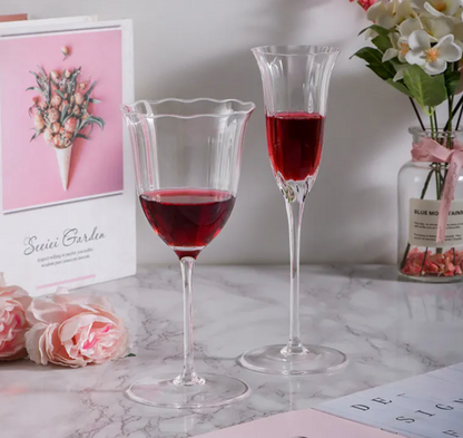 Two glasses of red wine on a marble surface with flowers and a card in the background.