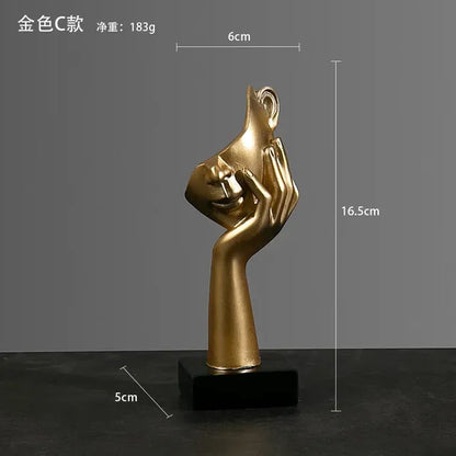 Gold sculpture of a hand covering a face on a black base with measurements indicated.