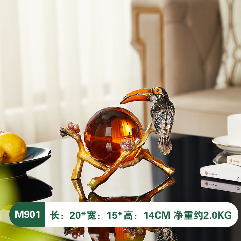 Decorative sculpture of a bird perched on a branch with a glass ball, placed on a surface.