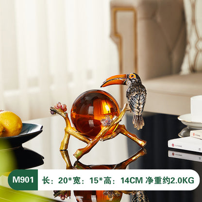 Decorative sculpture of a bird perched on a branch with a glass ball, placed on a surface.