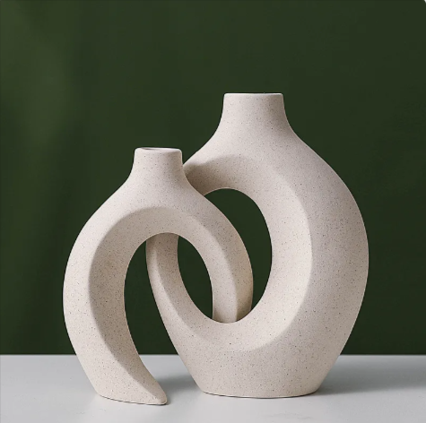 Two beige ceramic vases with circular design on a white surface and green background