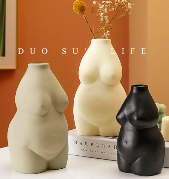Three unique vases shaped like women's bodies on a table with a blurred background.