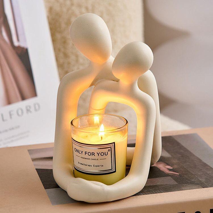 Ceramic sculpture of two figures holding a lit candle labeled 'Only For You' on a table.