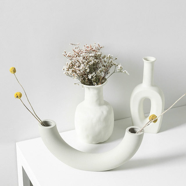 White ceramic vases with dried flowers on a light gray background