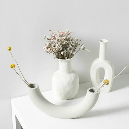 White ceramic vases with dried flowers on a light gray background