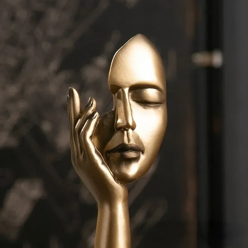 Gold mask and hand sculpture against a dark background