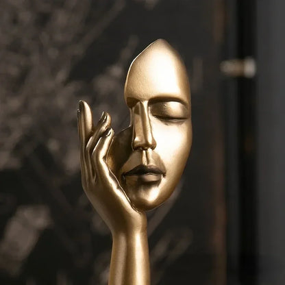 Gold mask and hand sculpture against a dark background