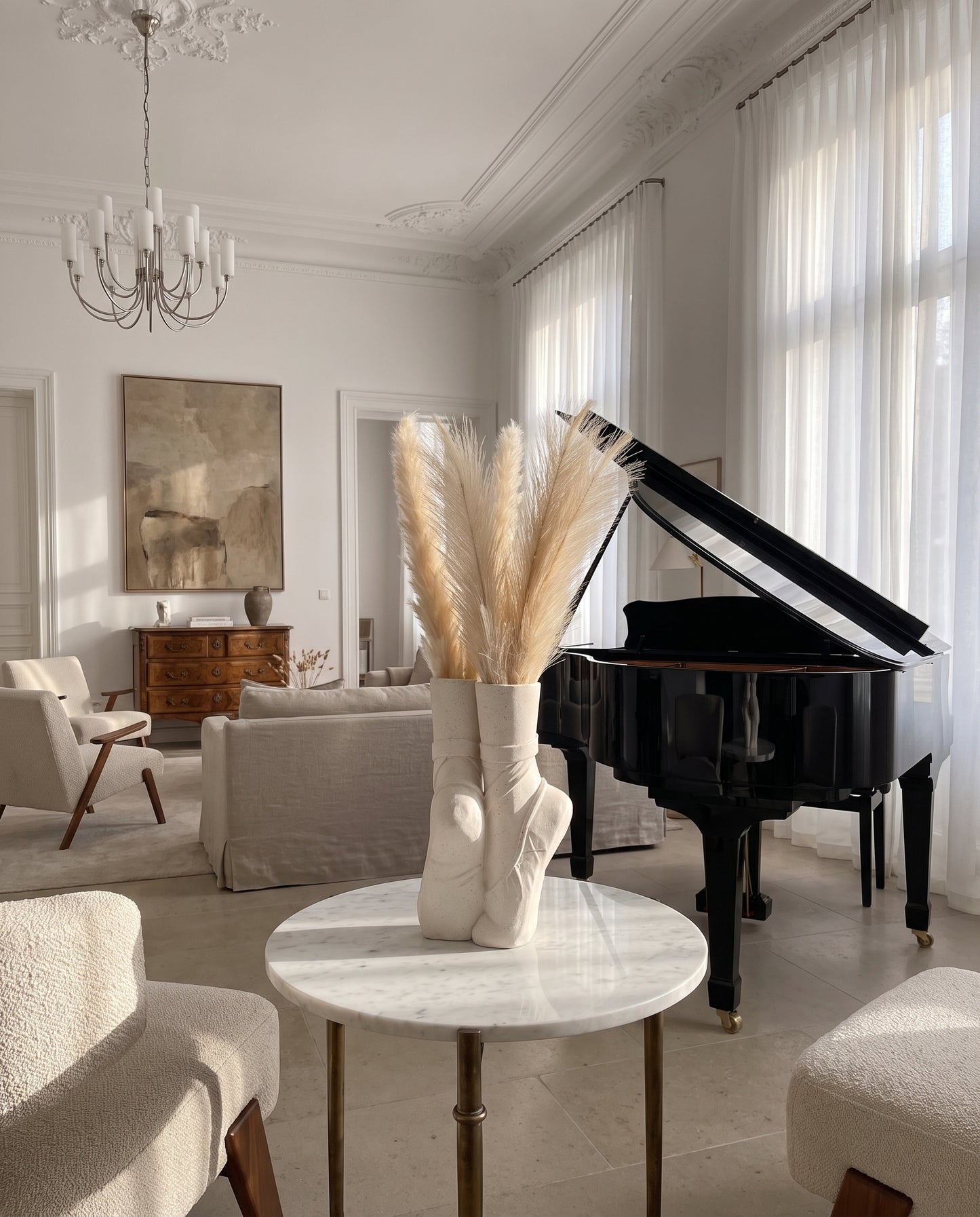 Elegant, sunlit living room featuring a grand piano, marble table with ballet shoe vase, and chic neutral decor.
